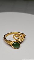 Front angled view of gold electroplated sterling silver ring with oval cabochon green jade and clear stones on leaf motif