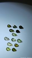 Photo showing 13 pear cut green tourmaline gemstones arranged in rows with varying green tones from pale to dark.