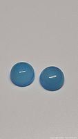 Photo of two round cabochon icy blue chalcedony stones on a neutral background showing their smooth domed surfaces and translucency.