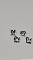 Four natural square cut aquamarine gemstones arranged on flat surface showing clarity and cut.