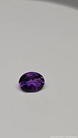 Oval deep purple Brazilian amethyst gemstone on a plain light surface, showing facets and reflective qualities.