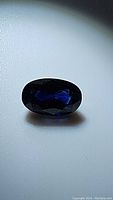 Top view of oval cut natural deep blue sapphire with visible facets and deep blue color under lighting.