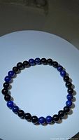 Top view of the black onyx and blue lapis lazuli gemstone bead bracelet laid flat in a circular form on white surface.