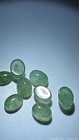 Eight green mint kyanite oval cabochon gemstones arranged loosely on a flat surface showing translucency and natural inclusions.