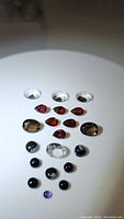 Top-down photo showing all 20 mixed faceted and cabochon cut gemstones on a white background arranged by type and color