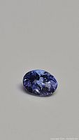 Oval cut natural tanzanite gemstone showing strong purple-blue color and faceting details on a neutral background.
