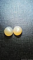 Pair of round peach moonstone cabochons on black textured background, showing color and sheen of stones.