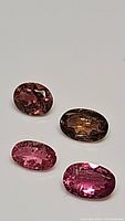 Four oval cut pink tourmaline gemstones shown from top angle on white background displaying varying pink hues and faceting.