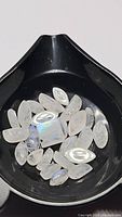 Parcel of 31 natural rainbow moonstones of various cuts including marquise, oval, and rectangular with visible blue flash in black container.