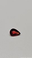 Pear-shaped deep fire red orange sapphire gemstone close-up on neutral background, showing color and facets detail.
