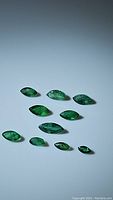 Image shows 10 natural green Zambian emerald gemstones, all marquis cut, arranged on white surface, highlighting their varying sizes and rich green color.