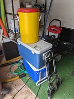 Overview showing all items stacked: yellow Igloo cooler on top, two rectangular coolers below, and folded cart leaning against coolers.