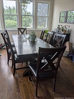 Full view of dark wooden rectangular dining table with six matching chairs around it in a room near windows.