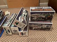 Multiple Hess toy vehicle boxes stacked on carpet showing the different models included in the lot