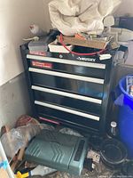 Full view of black metal Husky tool cabinet with 4 drawers. Various items placed on top, but not included in lot.