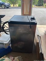 Side-front view of the stainless steel mini fridge with black top and attached power cord.