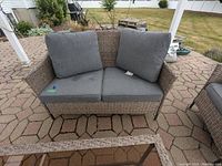 Front view of the Stylewell outdoor loveseat showing woven frame and gray cushions on a hexagonal stone patio.