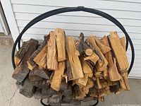 Front view of the metal circular log holder filled with stacked firewood, showing capacity and shape.