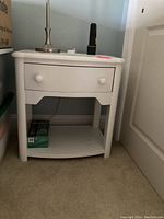 Nightstand viewed from front left angled perspective showing drawer, shelf, and contents not included below.