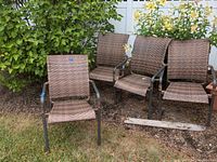 Wide shot showing all four woven outdoor patio chairs on grass near shrubs and fence.