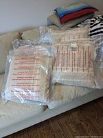 Four linen look pillows packaged in clear plastic sitting on a sofa, showing neutral beige covers with woven pattern.