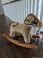 Side view of the plush rocking horse, showing brown fabric, wooden rocker, and brown bridle strap.