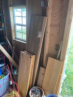 Flat scrap wood flat pieces leaning against a wooden wall near a window, stacked and varying in size and finish.