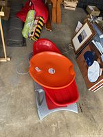 Three kids plastic snow sleds in garage: orange round saucer sled on top of a red toboggan sled, gray toboggan sled beneath both.