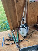 Photo capturing two Smith R200 sprayers and assorted yard tools including long handled loppers lying on wooden shed floor.