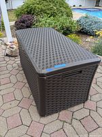 Dark brown rectangular outdoor storage container with woven rattan style texture on patio pavers, showing top and side view.