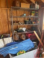 Overall view of metal wire shelving unit with garden items such as garden pots, sprays, folded blue patio umbrella, and storage tote below.