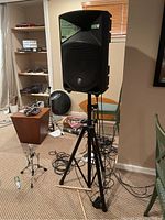 Single Thump speaker mounted on tripod stand with cables and drum hardware in background