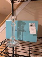 Photo of a clear Tiffany & Co. crystal candlestick showing faceted octagonal stem and wide multifaceted hexagonal base in front of a Tiffany & Co. blue box with logo.