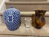Three vases shown on stairs: large blue and white oriental ceramic with lid, small clear glass vase in middle, amber glass vase on right.