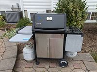 Front view of the Weber Genesis silver gas grill with closed lid, two propane tanks, and front cabinet doors.
