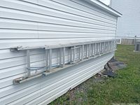 Side view of the 24-foot aluminum extension ladder leaning against house siding outdoors, showing length and two main sections.