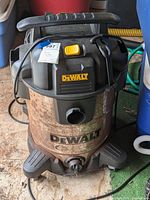 Full view of DeWalt wet dry vacuum showing yellow power switch, rusted metal tank, and black hose port below DEWALT logo