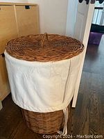 Full view of wicker hamper with cotton liner and a closed lid with handle.