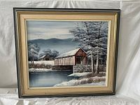 Front view of the oil painting depicting a covered bridge in winter, framed with a cream and black wooden frame.