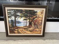 Frontal view of the oil painting showing the fall scenery with trees, path, and water under soft daylight, capturing the frame and artwork details.