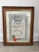 Front view of the framed certificate showing the entire document with visible water stains, aging, and original carved wooden frame with detailed edges.