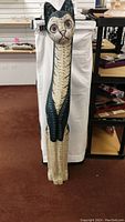 Full view of the tall wooden cat sculpture showing its height, painted details, and slender form.