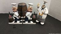 Photo of the front view of two chef bookends and one chef figure on a black surface with a white background.