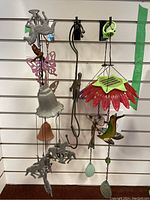 Photo showing multiple outdoor wind chimes hanging on slatwall including metal horses, butterflies, hummingbirds, flower-shaped chimes in red and purple, and bell-shaped terracotta chime.