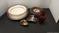 Wide view of the lot showing two Royal Vienna plates, one large bowl, red glass vase, two small red glass plates, and three decorative small plates with image and floral gold patterns.