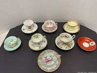 All seven assorted cups and saucers arranged on black background