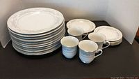 Stack of 11 dinner plates, 3 side plates, 4 cups and 4 saucers arranged on table showing floral border design