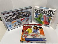 Photo showing the three boxed board games Richmond Opoly, Sorry!, and Frustration! set side-by-side.