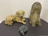Photo showing all three garden animal statues including two dogs and one turtle on a black surface with white background.