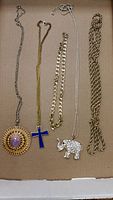 Five necklaces laid out side by side showing pendants and chains on a brown surface.